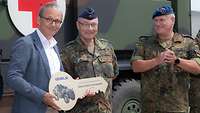 Ein zivil gekleideter Mann übergibt einen symbolischen Schlüssel an zwei Soldaten