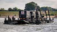Drei Lkw werden von einer Ponton-Fähre über den Rhein getragen.