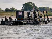Drei Lkw werden von einer Ponton-Fähre über den Rhein getragen.