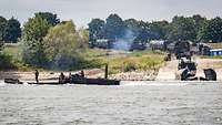 Lkw lassen Pontonteile zu Wasser, die auf dem Rhein zusammengekoppelt werden.