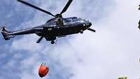 Ein blauer Hubschrauber der Bundespolizei fliegt. Er transportiert unter sich einen roten Behälter.