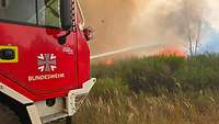 Ein Feuerwehrfahrzeug der Bundeswehr schießt einen Wasserstrahl auf das Feuer im Wald