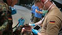Ein Mann in Uniform mit Stethoskop und ein Mann mit Tablet untersuchen einen Schwerstverletzten