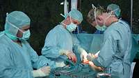 Drei Menschen in Klinikkitteln operieren 