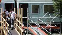 Vier Personen tragen einen Menschen auf einer Trage aus einem Zugwaggon