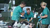Drei Sanitäter stehen um eine verletzte Person und behandeln diese unter anderem mit einer Infusion