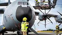 Eine Feuerwehrfrau steht vor dem Flugzeug und schaut zum Tragekorb am Cockpit des Flugzeuges.