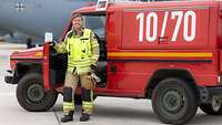 Eine Frau in Feuerwehruniform steht vor einem Einsatzfahrzeug und posiert für ein Foto.