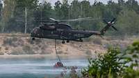 Ein Hubschrauber nimmt mit dem Löschwasserbehälter Wasser auf 