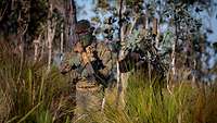 Zwei deutsche Soldaten mit Gewehren kämpfen in grünem, australischen Buschland bei Sonne.