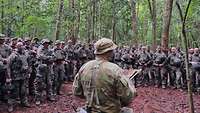 Zahlreiche deutsche Soldaten stehen vor einem australischen Soldaten im Dschungel.