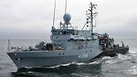 Ein kleines Schiff mit Soldaten und zivilen Besuchern an Bord fährt auf einem Gewässer