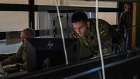 Zwei Soldaten sitzen in einem dunklen Raum an Computern und arbeiten.
