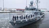 Ein kleines Schiff mit Soldaten an Deck läuft im Winter in einen Hafen ein