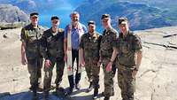 Ein Pfarrer und fünf Soldaten stehen auf einem Felsplateau