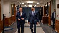 Boris Pistorius und Pete Hegseth laufen nebeneinander durch einen Gang auf den Betrachter zu.