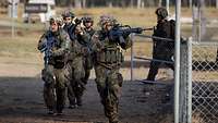 Viele Soldaten rennen mit Gewehren durch eine Straße und schießen dabei.