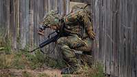 Ein Soldat klettert mit Ausrüstung durch ein Zaunloch.