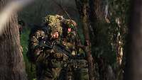Mehrere Soldaten stehen mit Waffen im Wald bei Sonnenaufgang. 