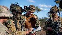 Mehrere Soldaten stehen im Gelände im Kreis. Einer hält eine Karte. Alle blicken drauf.