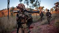 Viele Soldaten marschieren auf einem sandigen Weg im Buschland Australiens im Abendrot.
