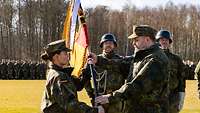 Vor Soldaten in Formation übergibt ein Offizier eine große Deutschlandfahne an eine Offizierin.