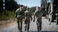 Drei Soldaten laufen, weg von der Kamera, den Schotterweg entlang der aufgereihten Waffensysteme.