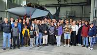 Menschen stehen in einem Hangar vor einen Eurofighter.