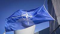 Eine blaue NATO-Flagge weht in den Masten eines grauen Schiffes.