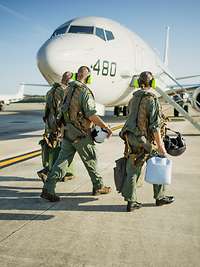 Drei Soldaten gehen auf dem Flugfeld zu einem parkenden Flugzeug vom Typ P-8A Poseidon