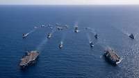 Luftaufnahme von Schiffen, die bei klarem Wetter in Formation über das Meer fahren