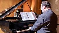 An einem schwarzen Flügel spielt ein Mann.