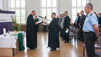 Zwei Pfarrer stehen sich vor einem Altar gegenüber, drumherum stehen Zivilisten und Soldaten.