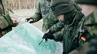 Mehrere Soldaten stehen im Feld um eine Karte herum und deuten auf unterschiedliche Punkte.