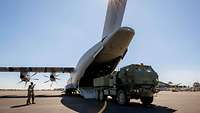 Ein massiger, grüner Lkw fährt rückwärts auf das geöffnete Heck eines Transportflugzeugs zu.