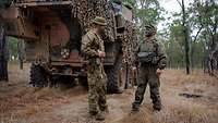 Ein australischer und ein deutscher Soldat sprechen miteinander, dahinter ein Gefechtsfahrzeug.