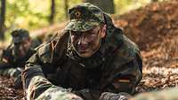 Ein Jugendlicher in Flecktarnuniform mit Tarnschminke kriecht auf dem Boden im Wald