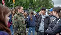 Soldatin im Gespräch am Hessentag 2024 Eine Soldatin spricht mit Jugendlichen. Im Hintergrund steht ein Hubschrauber.