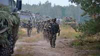 Getarnte Fahrzeuge und Soldaten, die sich in einer bewaldeten Landschaft bewegen.