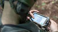 Nahaufnahme eines Soldaten von hinten, der auf den Monitor eines mobilen Geräts schaut.