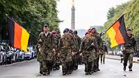 Marsch zum Gedenken in Berlin Soldaten marschieren mit Deutschlandflaggen auf einer Straße. Im Hintergrund ist die Siegessäule zu sehen.