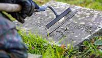 Ein Soldat reinigt mit einem Gartengerät einen Grabstein