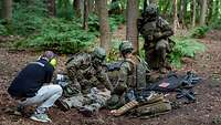 Spracherkennung für die Digitalisierung der Rettungskette Zwei Soldaten versorgen einen Verwundeten im Wald. Ein Mann kniet daneben und filmt sie dabei.