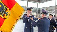 Ein Soldat übergibt in einem Hangar an einen anderen Soldaten die Truppenfahne.
