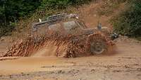 Geländewagen Wolf 2 – der digitale Pionier im Test Ein Geländewagen Wolf 2 fährt im Gelände durch eine tiefe Pfütze und Schlamm spritzt hoch