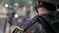 Ein Soldat mit silberner Kordel und zitronengelber Litze an der Schulterklappe des Feldanzugs