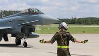 Ein Kampfjet vom Typ Eurofighter fährt am Boden und ein Soldat weißt ihn ein.