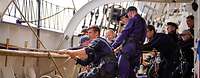 Mehrere Soldaten ziehen an einem Tau, an Bord eines Segelschiffs.