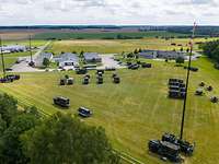 Aus der Luft betrachtet stehen mehrere militärische Fahrzeuge, einige mit Antennen, auf einer Wiese.