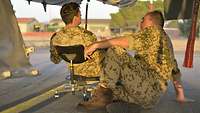 Ein Pfarrer sitzt auf dem Fußboden und spricht mit einem Soldaten, der auf einem Stuhl sitzt.
